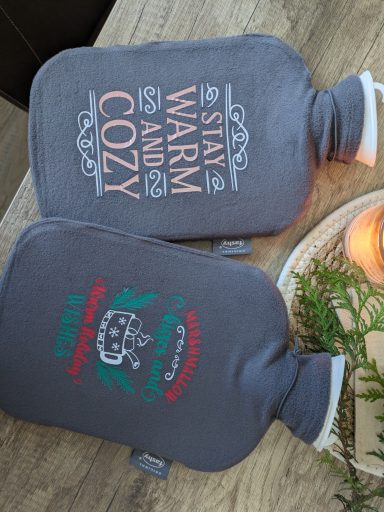 Wärmflaschen beplottert Zwei Wärmflaschen mit den Aufschriften "Stay Warm" und "Cozy".